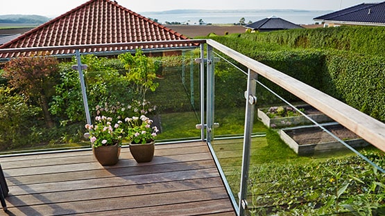 Terrasse med glasgelænder og fin udsigt over have, huse og havet